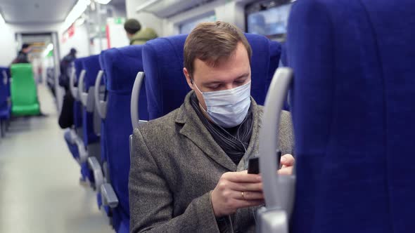 Millennial Man in Mask Commuting on Train Sitting Listening to Music on Mobile Phone alt