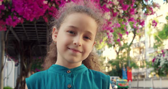 Portrait Cute Little Child Girl Looking at Camera Standing on Street in City on Summer Day alt