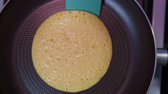 Turning To The Other Side a Round Pancake in Frying Pan with Silicone Spatula