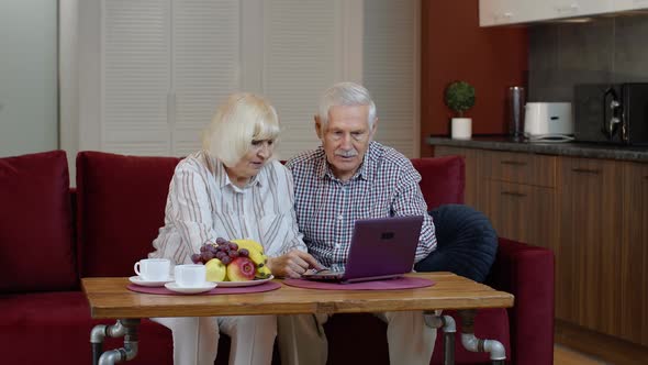 Senior Pensioner Couple with Digital Laptop Pc Computer at Home. Resting on Sofa in Cozy Living Room alt