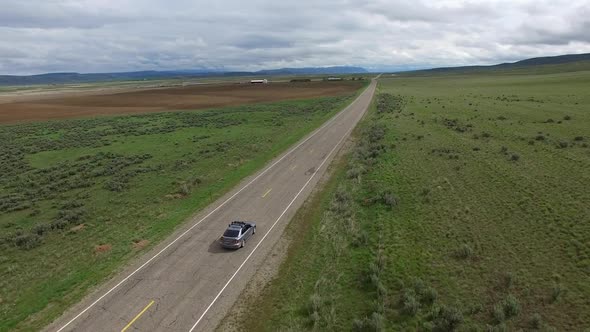 Drone following car on road in a vast landscape alt