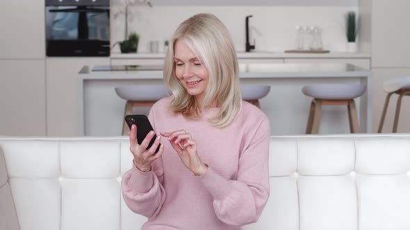 Happy Grey Haired Senior Woman Holding Smart Phone Looking at Cellphone Screen Playing Mobile Games alt