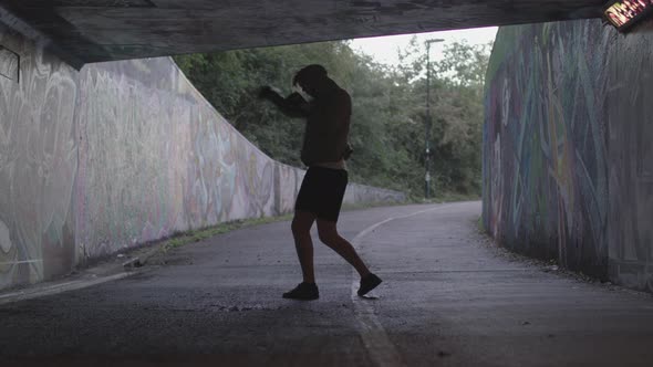 Wide Shot of a Young Athletic Man Boxing in an Underpass, Silhouetted By The Light Behind Him - Ungr alt