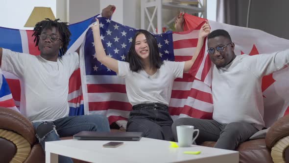 Cheerful Friends Posing with Flags Indoors Sitting on Comfortable Couch in Living Room alt