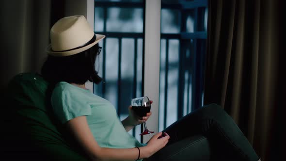 Brunette Girl in a Hat Drinks Wine and Looks Out the Window at Home Bad Weather Cinematic Shot