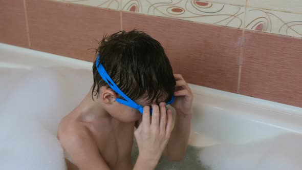 Boy 6-7 Years Sitting in the Bubble Bath and Trying To Wear Goggles.