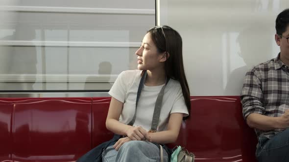 Asian female tourist sitting and sightseeing urban window view in public train. alt