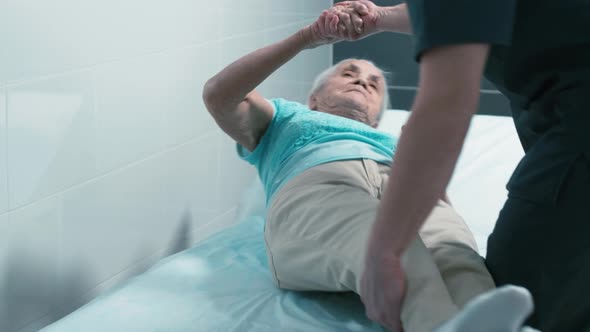 Aged woman sitting on therapy bed with doctor's help