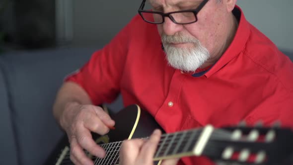 An Elderly Man in a Red Shirt and Glasses Plays an Acoustic Guitar alt