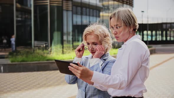 Female Coworkers Discussing Over Tablet While Standing Outside Office Building