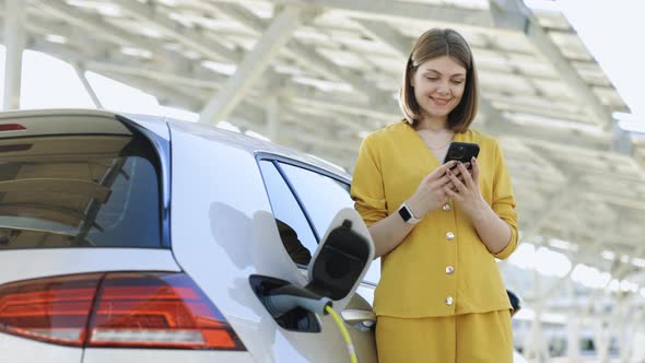 Woman Use Smart Phone While Waiting and Power Supply Connect to Electric Vehicles for Charging