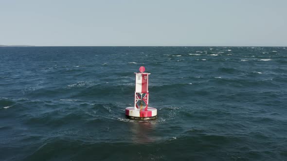 Aerial View of the Buoy Within the Bluish Sea Waves and Autumn Forest Behind alt