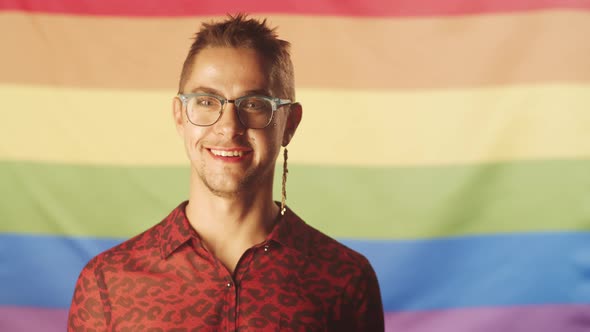Joyous Gay Man with Makeup Posing against Pride Flag alt