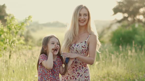 Smiling Blonde Mom in a Summer Dress Combs Her Daughter's Hair