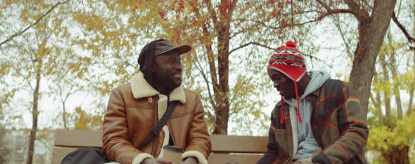 African American Men Chatting over Coffee on Bench in Park alt