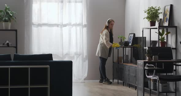 Young Housewife with Headphones Is Doing Cleanup in Living Room Clearness and Coziness at Home alt