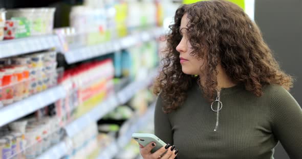 Young Attractive Woman Checking to Do List on Smartphone in Supermarket alt