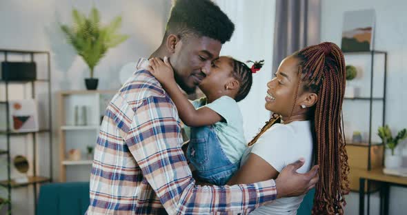 Happy African Parents Kissing and Embracing Daughter alt