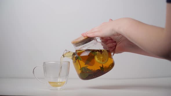 Pouring citrus mint tea from a clear glass teapot into a double walled cup.