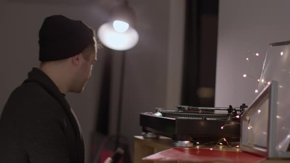 Young Unshaven Handsome Guy Takes Record Off Turntable Taking His Headphones Off