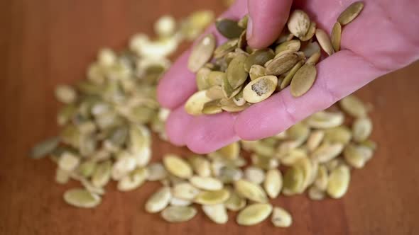A Lot of Raw Pumpkin Seeds Fall From Female Hands on the Table alt