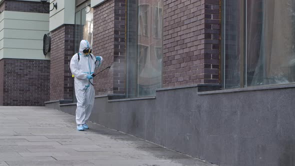 A Virologist in a Protective Suit Disinfects the Surface, Sprays Liquid Chemicals Near the Business alt