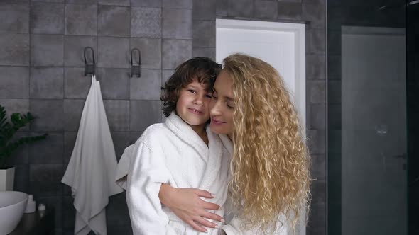 Smiling Happy Mother and Son in Dressing Gowns which Looking at Camera in the Bathroom alt