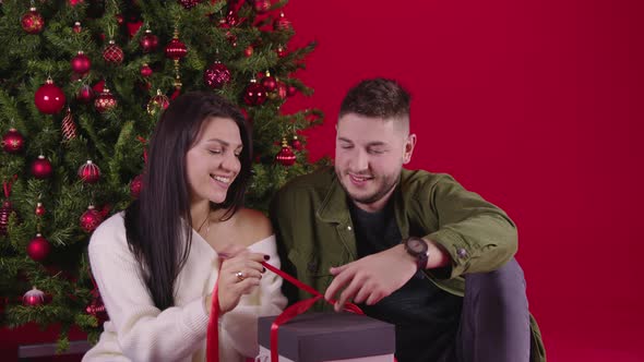 Young Loving Couple Opening Long Awaited New Year Gift Sitting Near Xmas Tree