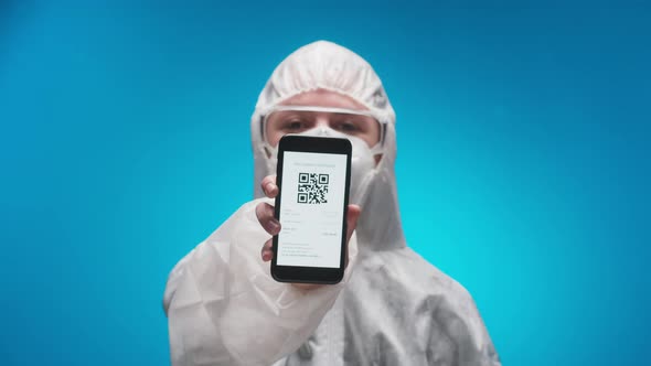 Woman Doctor Wearing Protective Uniform Showing on Phone Vaccination Passport with Qr Code alt