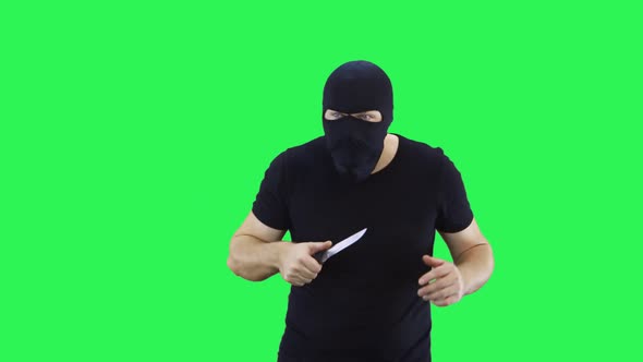 A man in a black mask holds a sneaking knife in his hand.Balaclava.Green screen background.