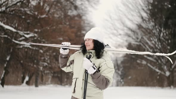 Sporty Mature Woman with Skis Standing in Forest in Winter alt