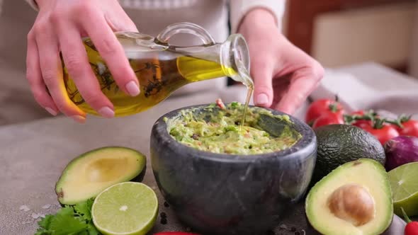 Making Guacamole Sauce  Woman Pouring Olive Oil Into Mixed Ingredients in Marble Bowl Mortar alt