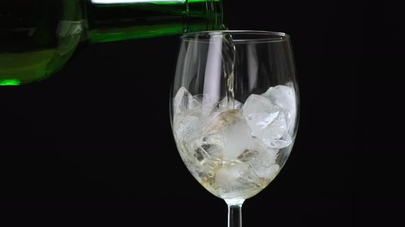 Pouring white wine in glass with ice cubes on black. 4k