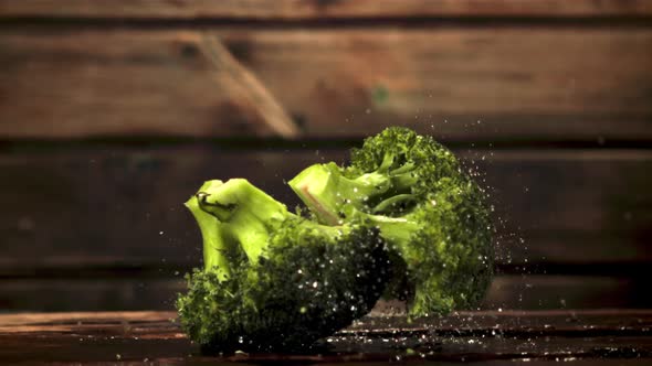 Super Slow Motion Pieces of Broccoli Fall on the Table with Splashes of Water alt