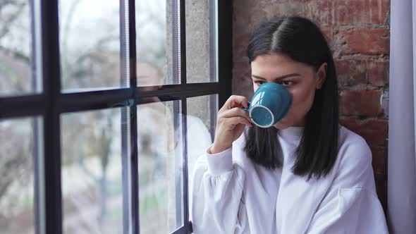 Beautiful Happy Caucasian Brunette Sitting Next to the Window Drinking Tea and Enjoying Her Day alt