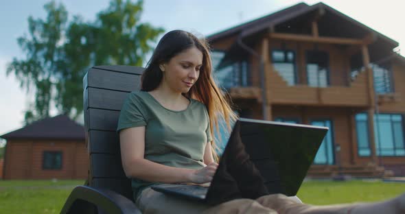 Young Beautiful Girl Working on Laptop in Backyard of Country House alt