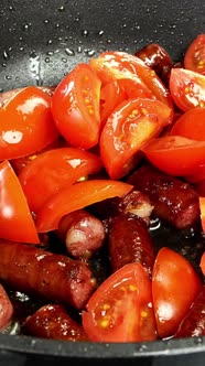 Delicious Fatty Hunting Sausages Cut Into Pieces and Sliced Tomato are Fried in Frying Pan alt