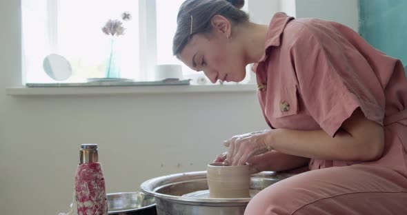 Female Potter Sitting and Makes a Cup on the Pottery Wheel. Woman Making Ceramic Item. Pottery alt