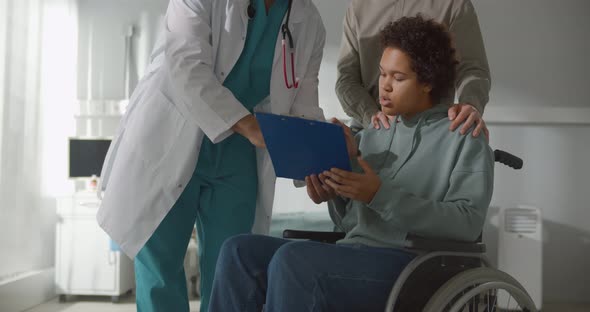 Young African Woman Patient in Wheelchair Signing Discharge Documents at Hospital Ward alt
