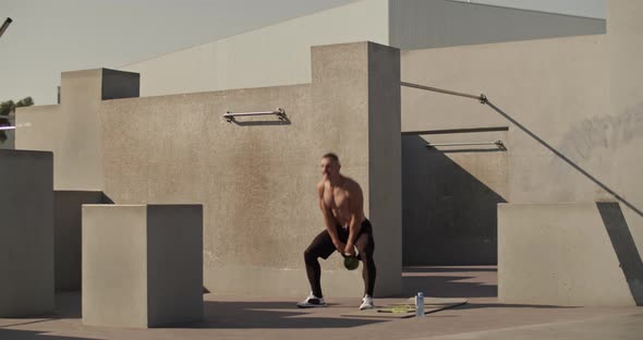 Sportsman Exercising with Kettlebell Outside Concrete Building alt