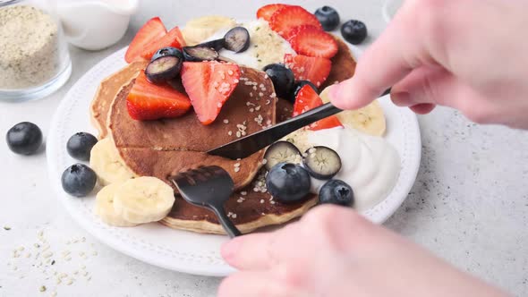 Eating pancakes with strawberries, blueberries, banana and cream on white plate. alt