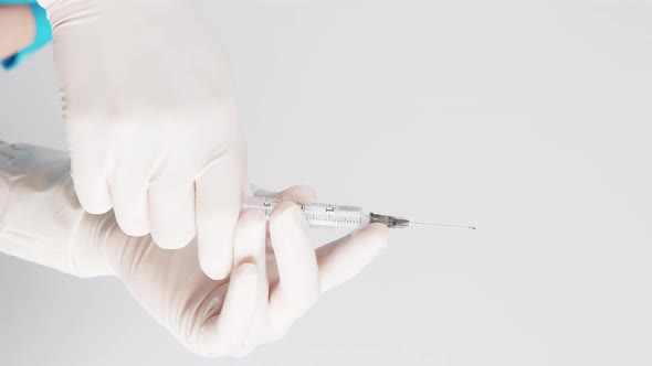 Vertical Shot of Two Hands in White Protective Gloves Preparing Syringe with the Vaccine Over White alt