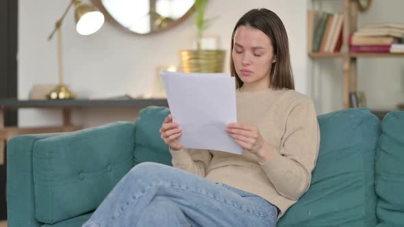 Young Woman with Documents Reacting to Loss on Sofa alt