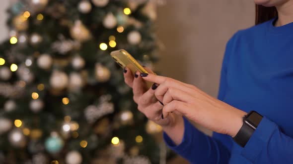 Woman Sitting with a Phone in Her Hands on a Christmas Tree on a Holiday alt