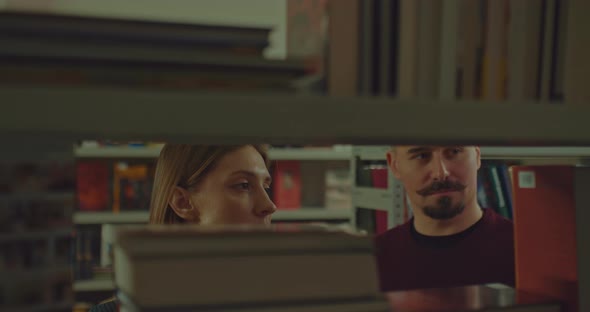 Beautiful Woman and a Man are Standing at the Bookshelves of the Library Choosing Books alt