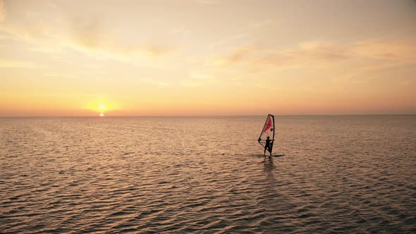 Distant Person Sails Windsurf Board on Ocean at Sunset
