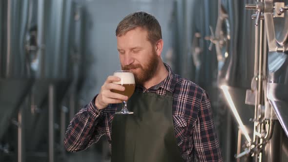 Portrait. An Adult Male Brewer Checks the Color of Freshly Brewed Beer From a Beer Tank While alt