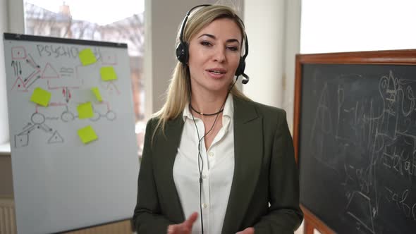 Portrait of Confident Woman in Headphones Talking Looking at Camera Standing in Classroom with alt