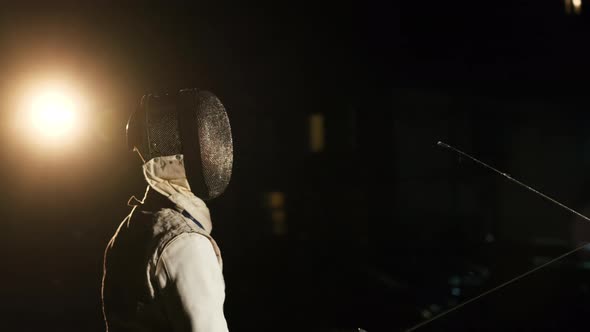 Two Fencers In Fencing Suits And Helmets Fencing In The Dark Outside. alt