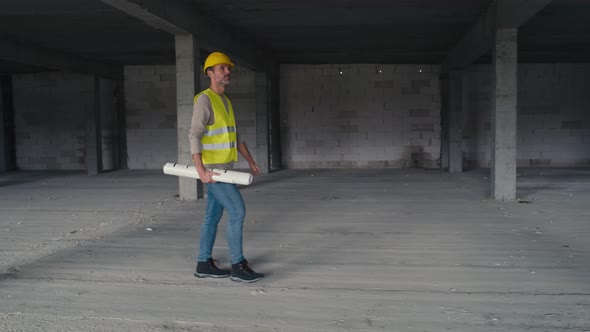 Wide image of caucasian engineer walking on construction site and holding project plans. alt